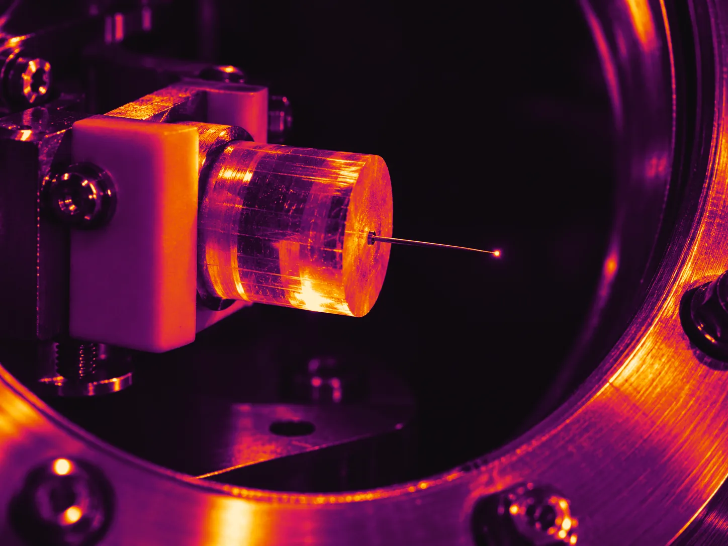 Illustrative photograph: a polished cylindrical crystal with a fine tungsten needle and a faint point of glow in a vacuum chamber